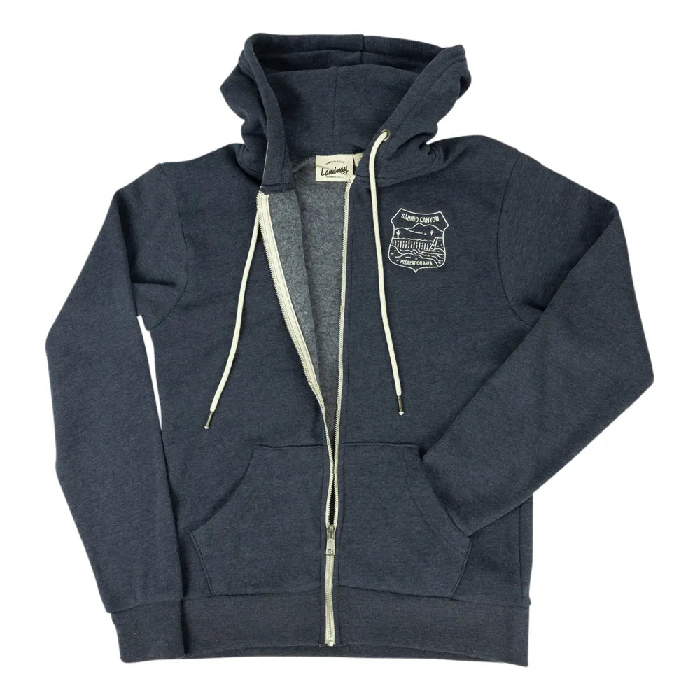 A dark heather gray zip-up hoodie with cream-colored drawstrings and a white embroidered shield logo on the left chest, displayed flat against a white background.