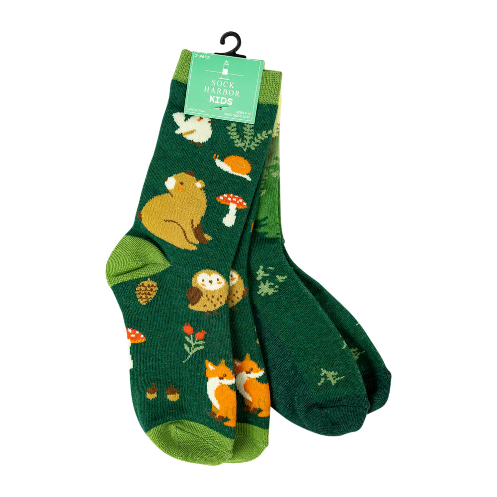 A pair of children's crew socks from Rock Harbor Kids, featuring a forest theme with woodland animals like a bear, owl, fox, and mushroom on a dark green background, complete with a green hanger tag.
