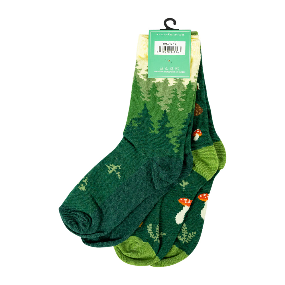 A pair of forest-themed crew socks with a green pine tree pattern and small red-and-white mushrooms, shown hanging from a green retail tag on a white background.