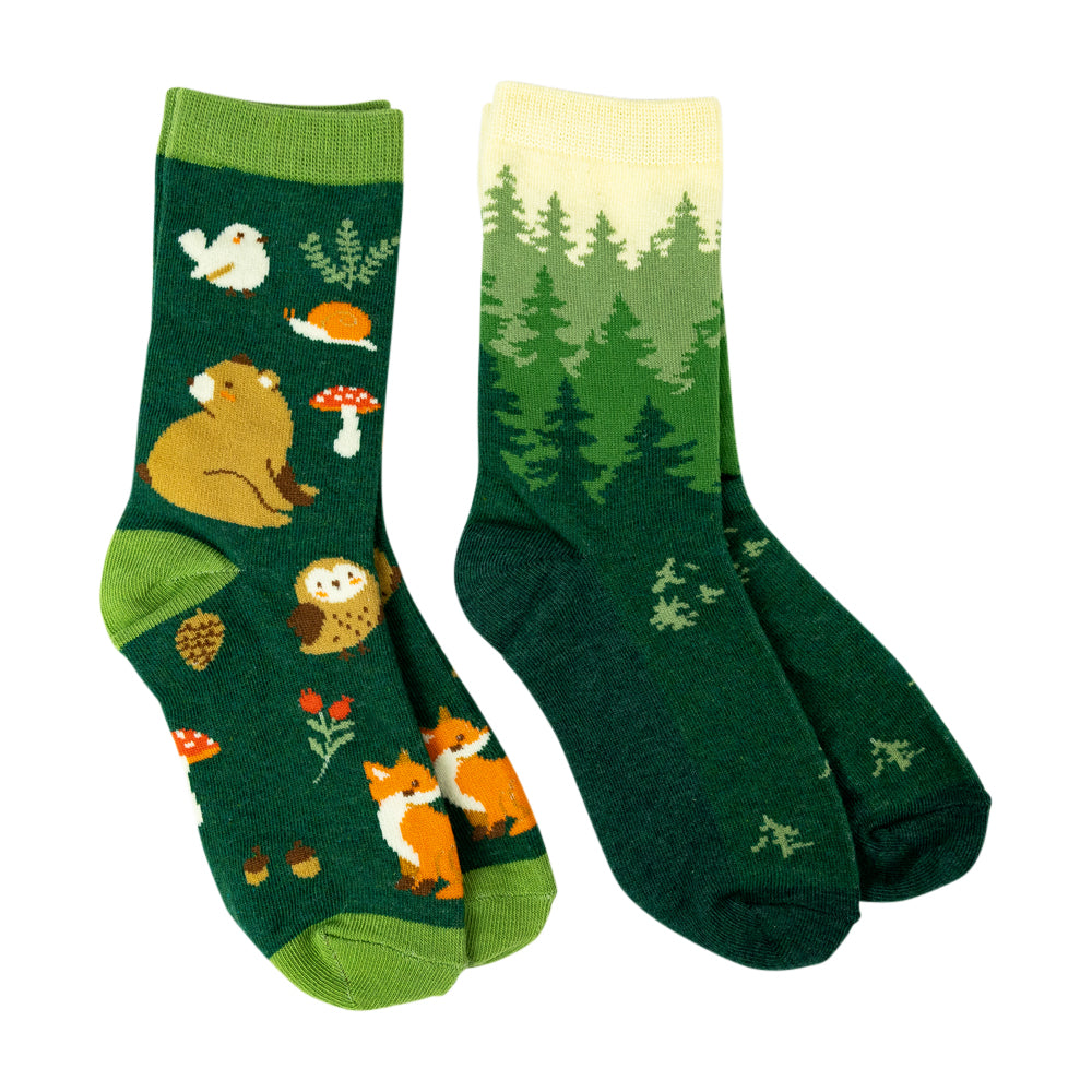 A pair of forest-themed crew socks displayed against a solid white background. One sock features a dark green base with whimsical woodland illustrations including a brown bear, a white bird, a red-and-white mushroom, and an orange fox.