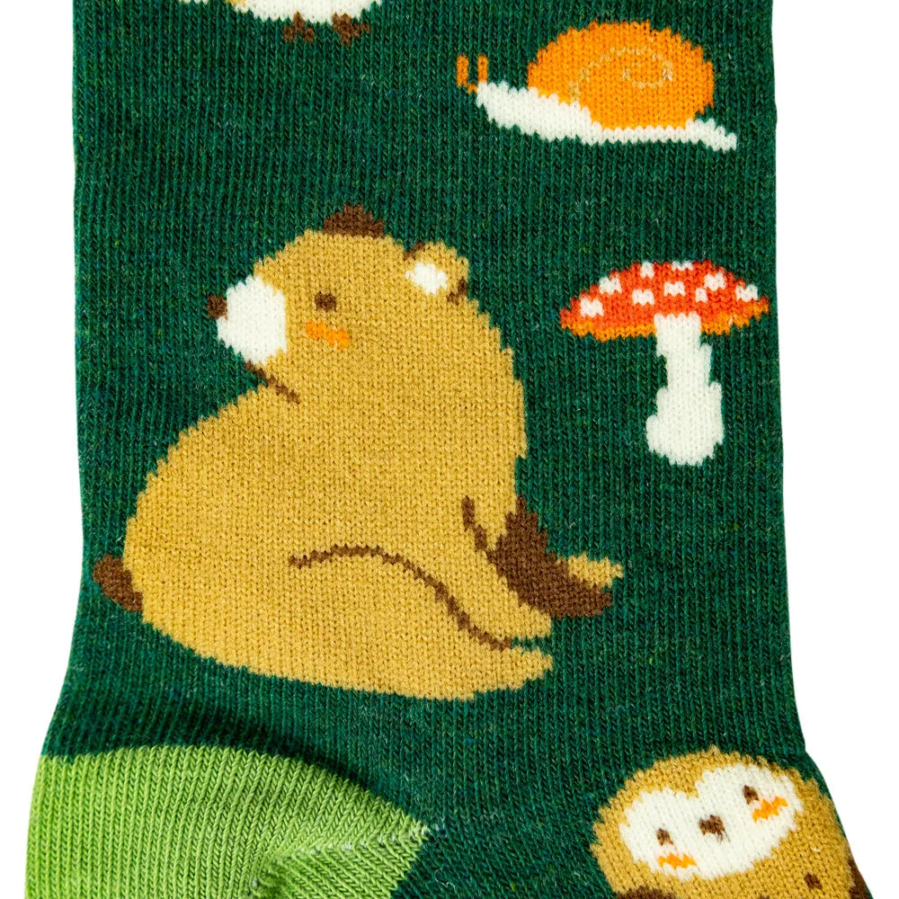 A close-up of a dark green knit sock featuring a playful woodland pattern with a large tan bear, a red-and-white mushroom, a white snail, and a green heel area.