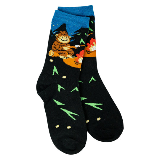 A pair of black crew socks with a colorful Bigfoot camping graphic on the upper leg and green pine tree patterns on the feet, shown against a plain white background.