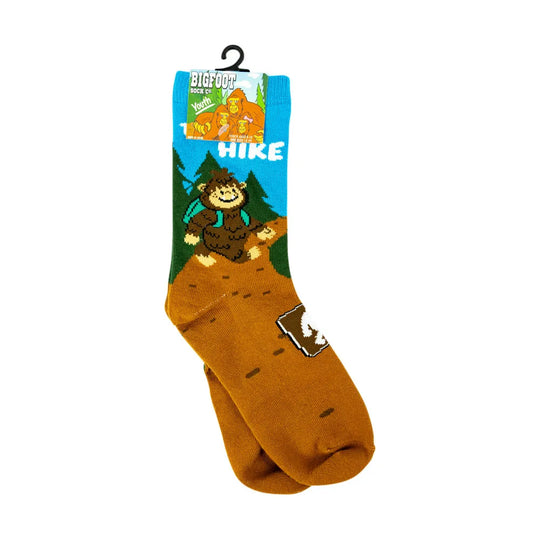 A pair of brown hiking socks with a cartoon Bigfoot graphic on the cuff and a small bear paw print on the side, hanging from a black plastic hanger against a white background.