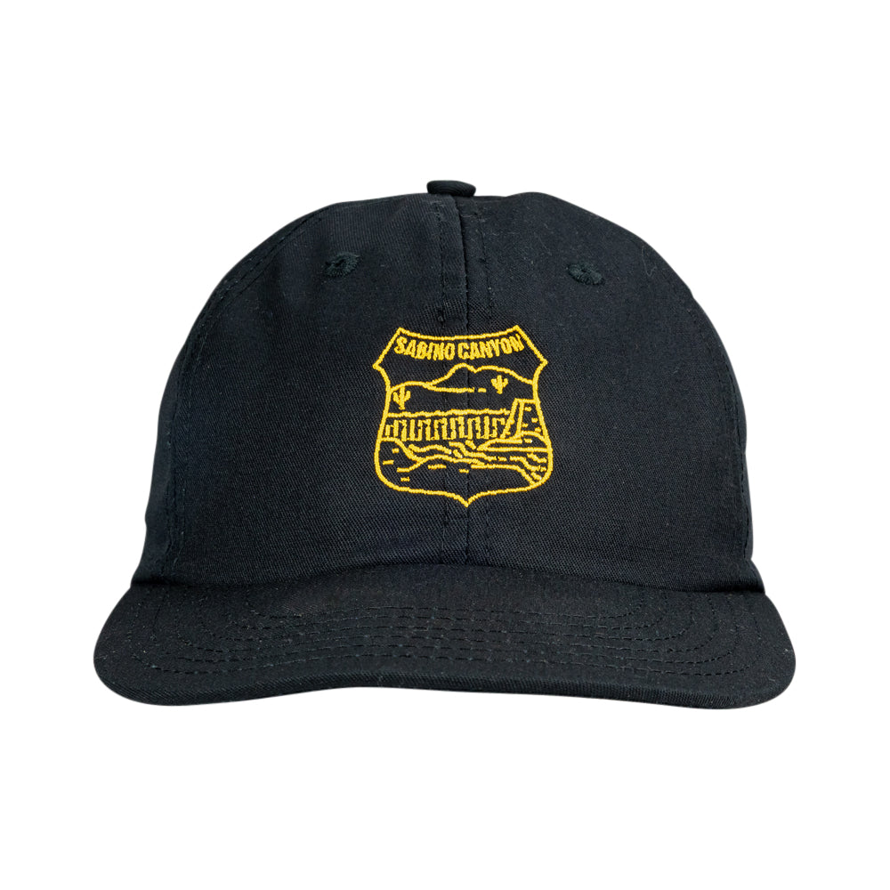A black baseball cap featuring a yellow embroidered shield logo on the front with the text &