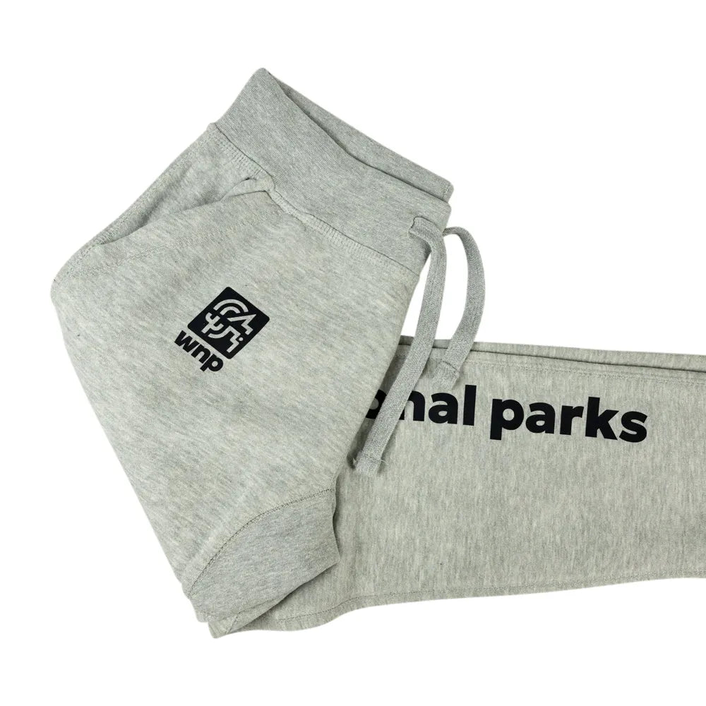Light heather gray sweatpants folded to show a black square logo patch on the leg and black text reading &