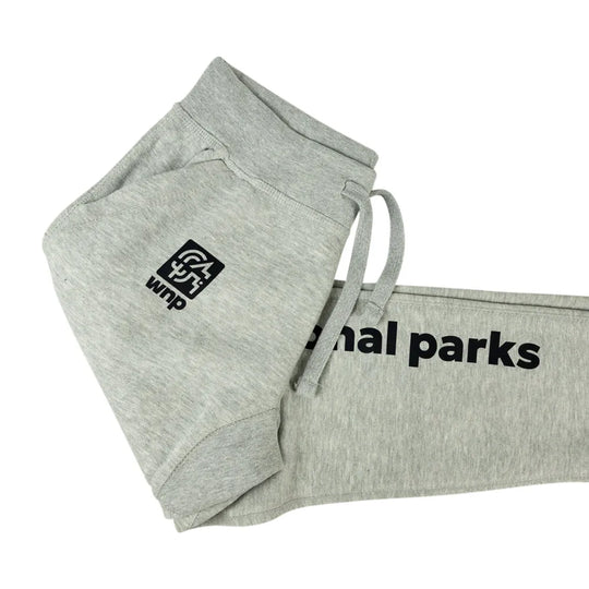 Light heather gray sweatpants folded to show a black square logo patch on the leg and black text reading &