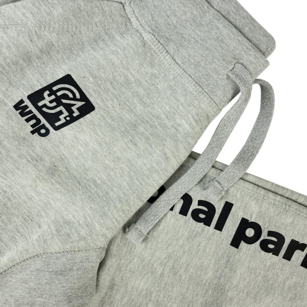 Close-up of light heather gray sweatpants with black printed branding and partial text on the leg, plus matching drawstrings and a ribbed waistband, shown on a white background.