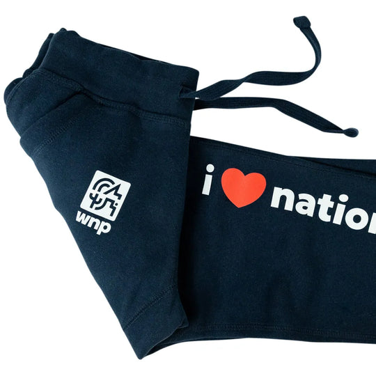 A pair of navy blue sweatpants folded on a white background, featuring a white square logo on one leg and &