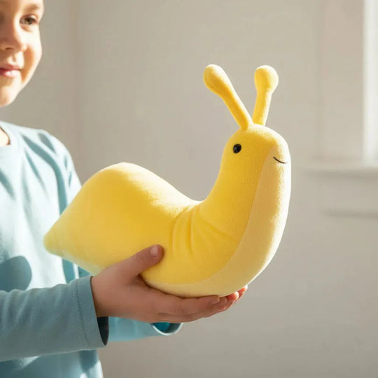 A yellow plush snail toy with two antennae, a small embroidered smile, and a black bead eye being held by a small child in a blue shirt