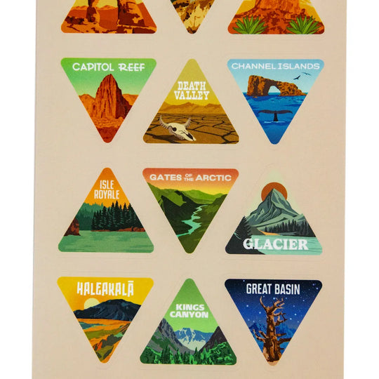 A sheet of triangular travel-themed stickers featuring illustrated landscapes and place names including Capitol Reef, Channel Islands, Death Valley, Isle Royale, Gates of the Arctic, Glacier, Haleakala, Kings Canyon, and Great Basin on a light beige background.