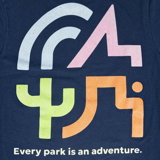 Close-up of a navy blue graphic T-shirt featuring stylized letters and shapes in white, pink, lime green, and orange, with the phrase &