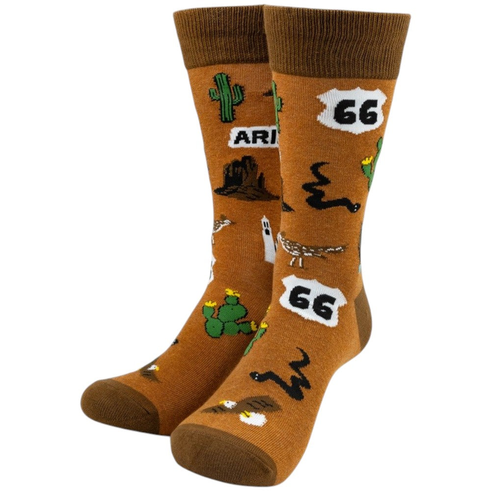 A pair of brown crew socks with a desert-themed pattern featuring cacti, a rock formation, a road sign reading &
