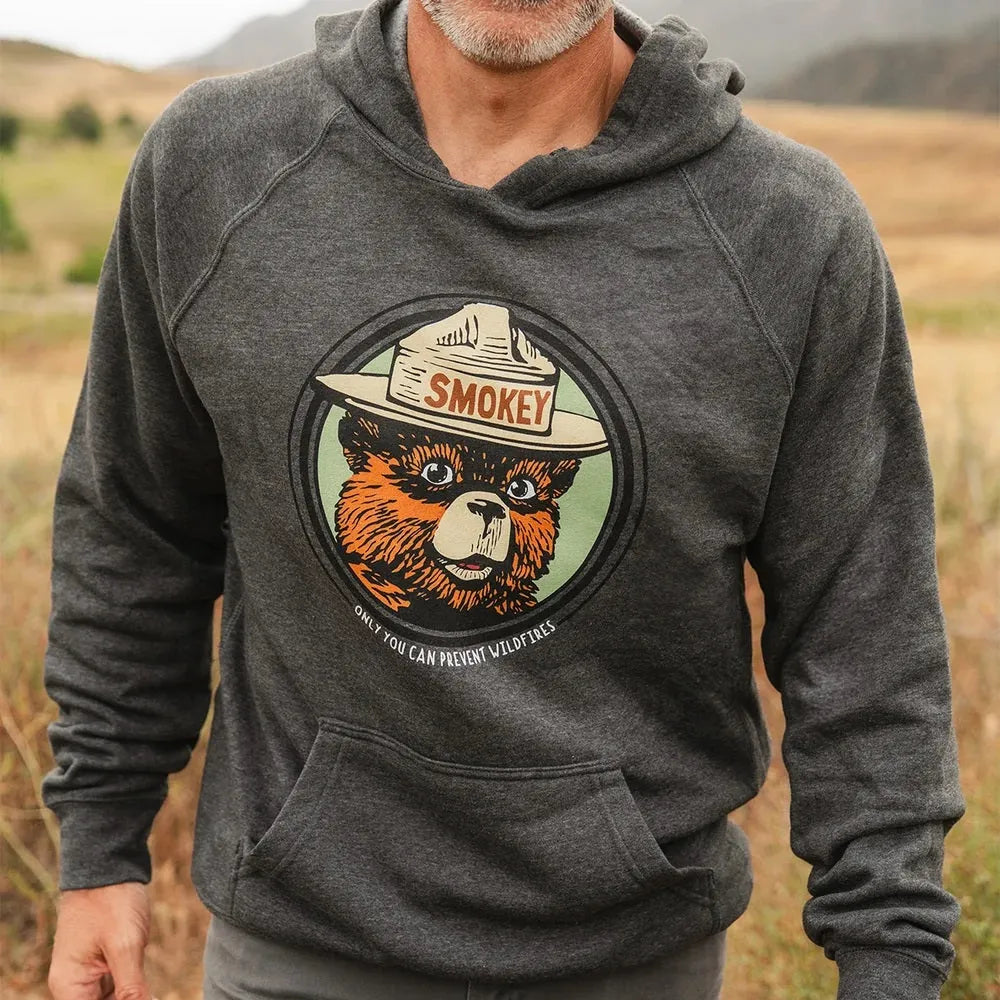 Close up of a person wearing a charcoal gray Smokey Bear hoodie with vintage bear face graphic and “Only You Can Prevent Wildfires” text.