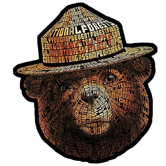 A die-cut sticker or decal featuring Smokey Bear and hat design made from layered text. The bear face and hat are filled with many words in black, brown, orange, and red tones, outlined by a thick black border on a plain white background.