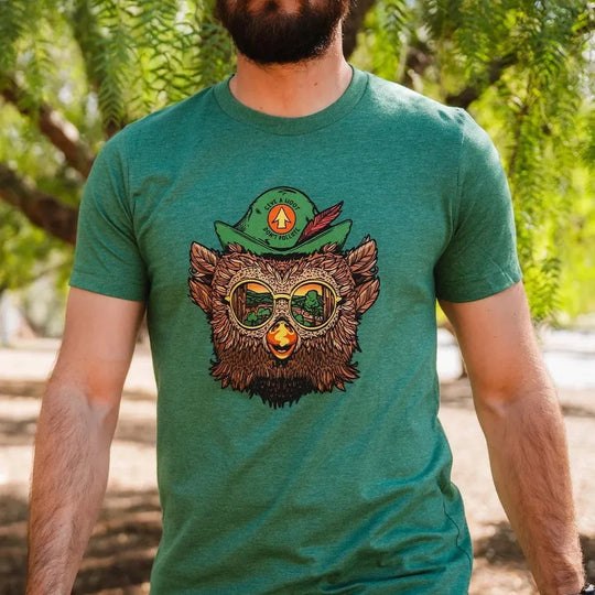 Close up of a person wearing a Woodsy Owl t-shirt. The graphic on the front is an illustration of Woodsy Owl wearing sunglasses reflecting a forest scene and a feathered cap that says "Give a Hoot, Don&