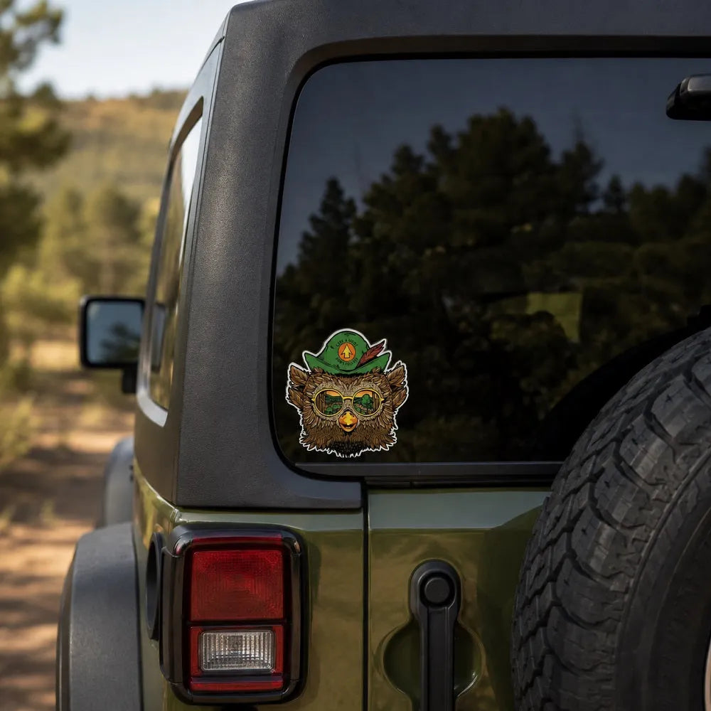 A sticker of Woodsy Owl wearing a green hat and glasses, applied to the back window of an olive green vehicle on a dirt road.