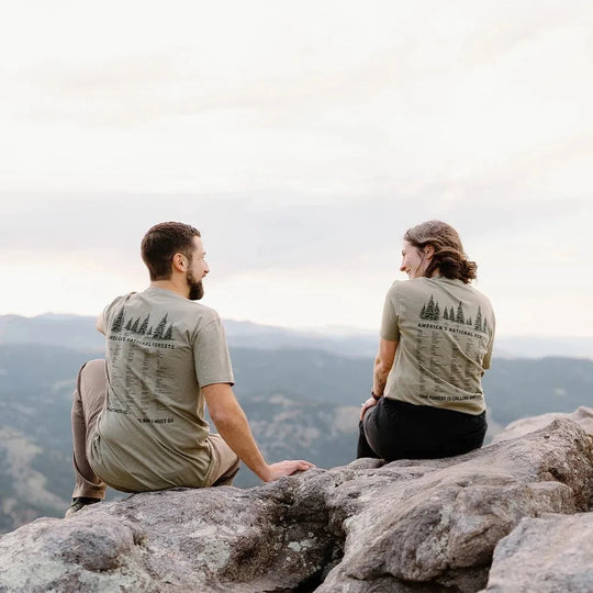 Two people sitting on a mountain top wearing matching t-shirts with nature-themed designs.