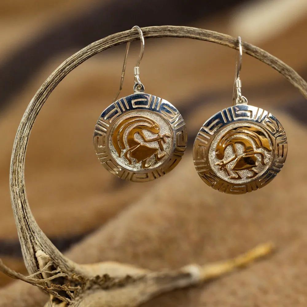 Pair of gold and silver earrings on a branch with a blurred natural background