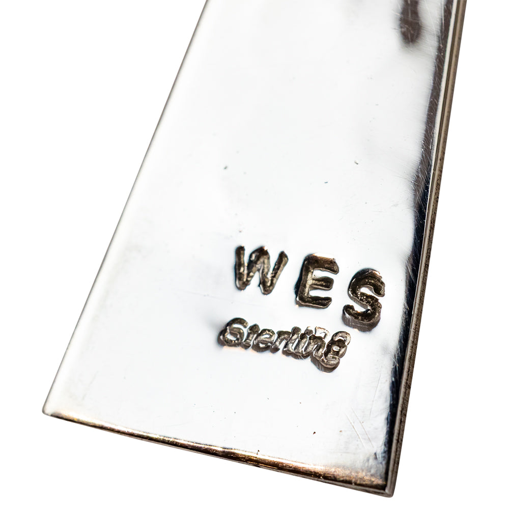 Close-up of a silver pendant with 'WES Sterling' engraving on a white background