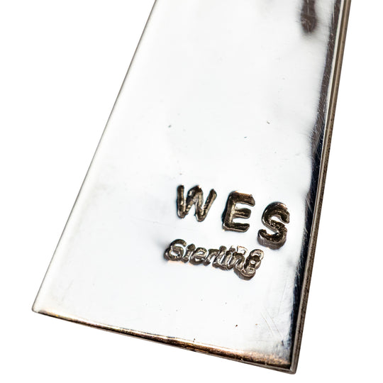 Close-up of a silver pendant with 'WES Sterling' engraving on a white background