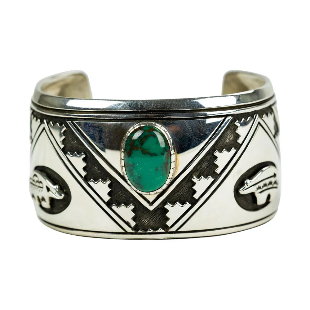 Silver cuff bracelet with green stone and tribal designs on a white background