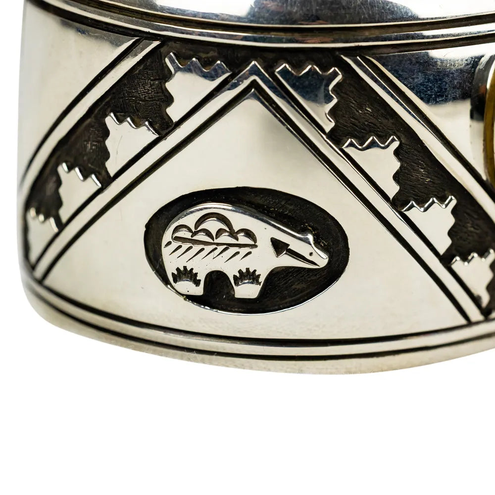 Silver Navajo bracelet with bear emblem and geometric patterns on a white background