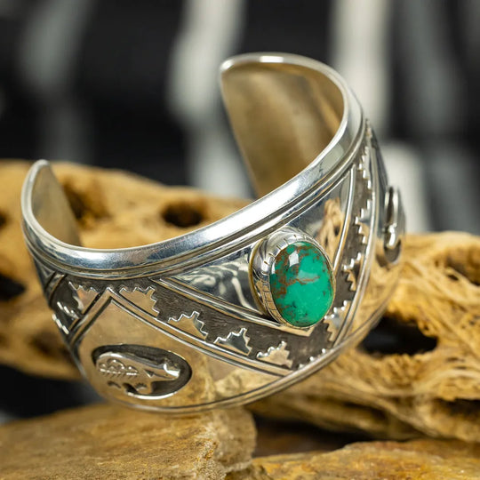 Silver cuff bracelet with green stone on a textured surface