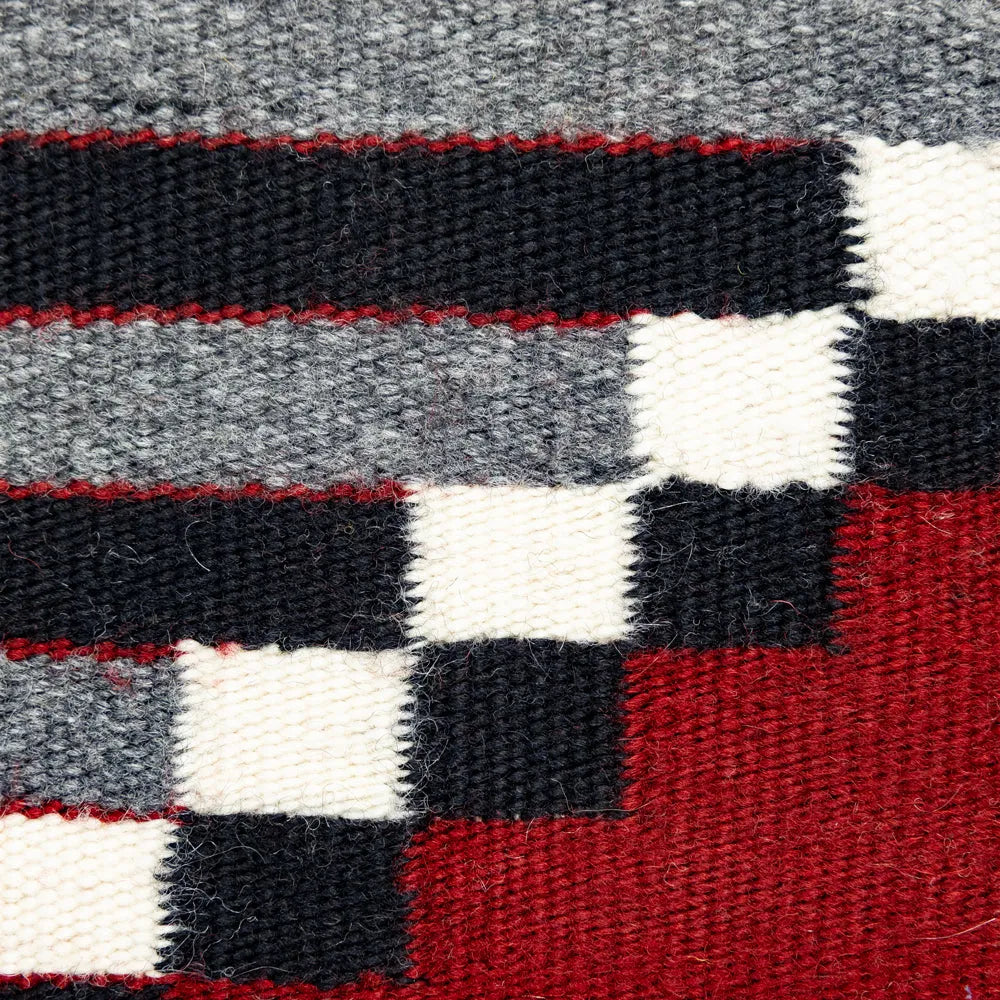 Close-up of a woven fabric with red, black, and white stripes on a gray background.