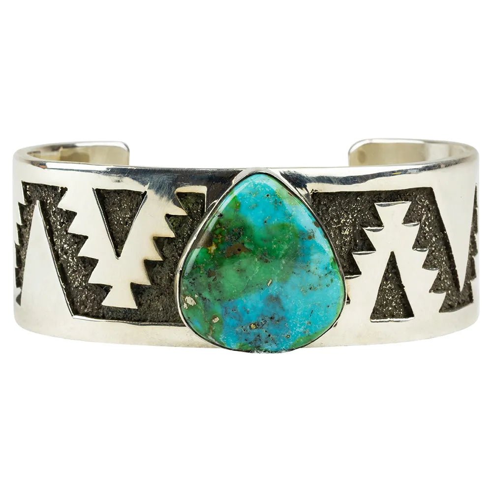Closeup view of silver cuff bracelet with turquoise stone and geometric pattern on a white background