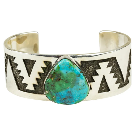 Silver cuff bracelet with turquoise stone and geometric designs on a white background