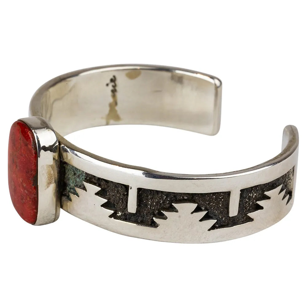 Silver Navajo bracelet with red stone and geometric design on a white background