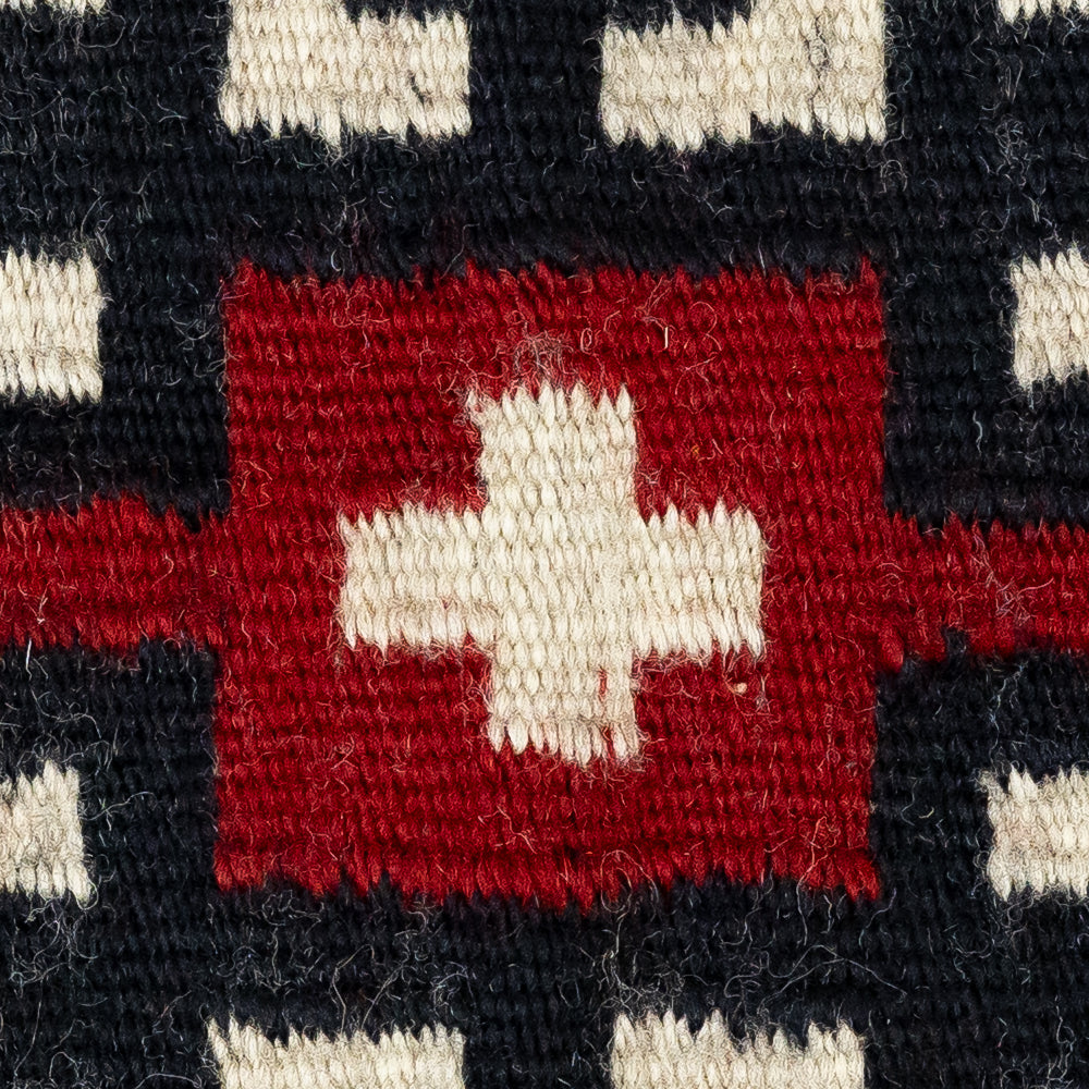 Close-up of a woven fabric with a red square and white cross pattern on a black background.