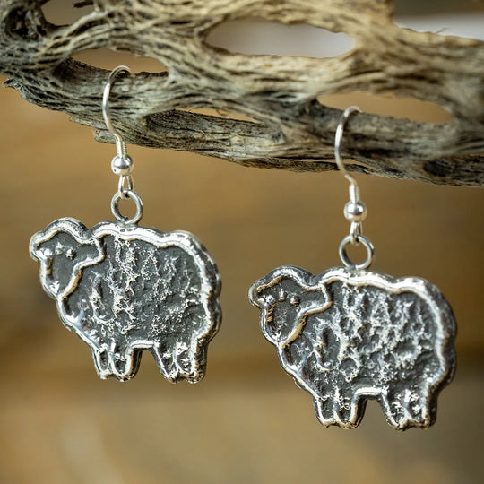 Silver sheep-shaped tufa cast earrings on a natural wood background