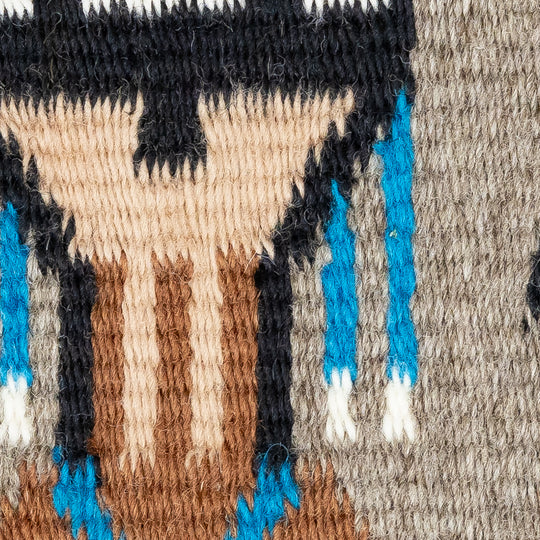 Close-up of a woven textile with geometric pattern featuring black, blue, brown, and beige colors.