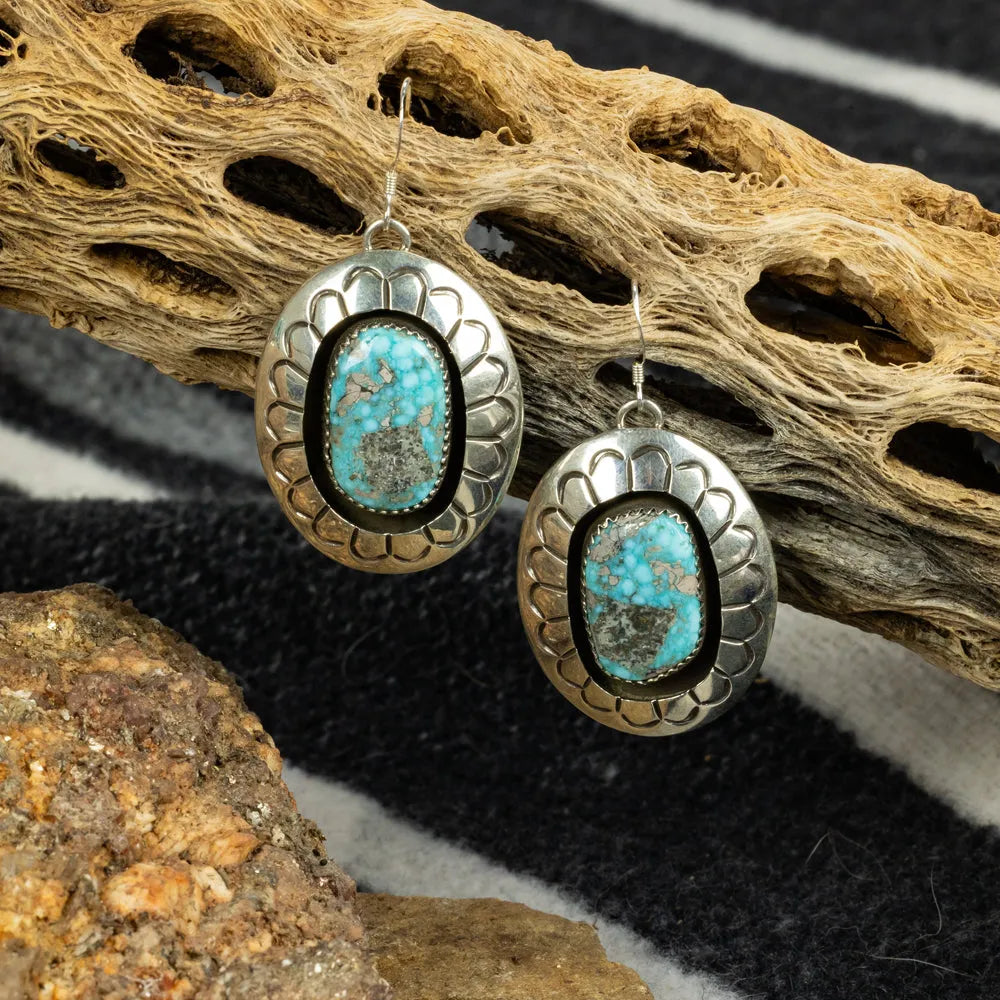 Silver earrings with turquoise stones on a textured surface