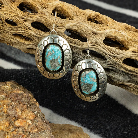 Silver earrings with turquoise stones on a textured surface