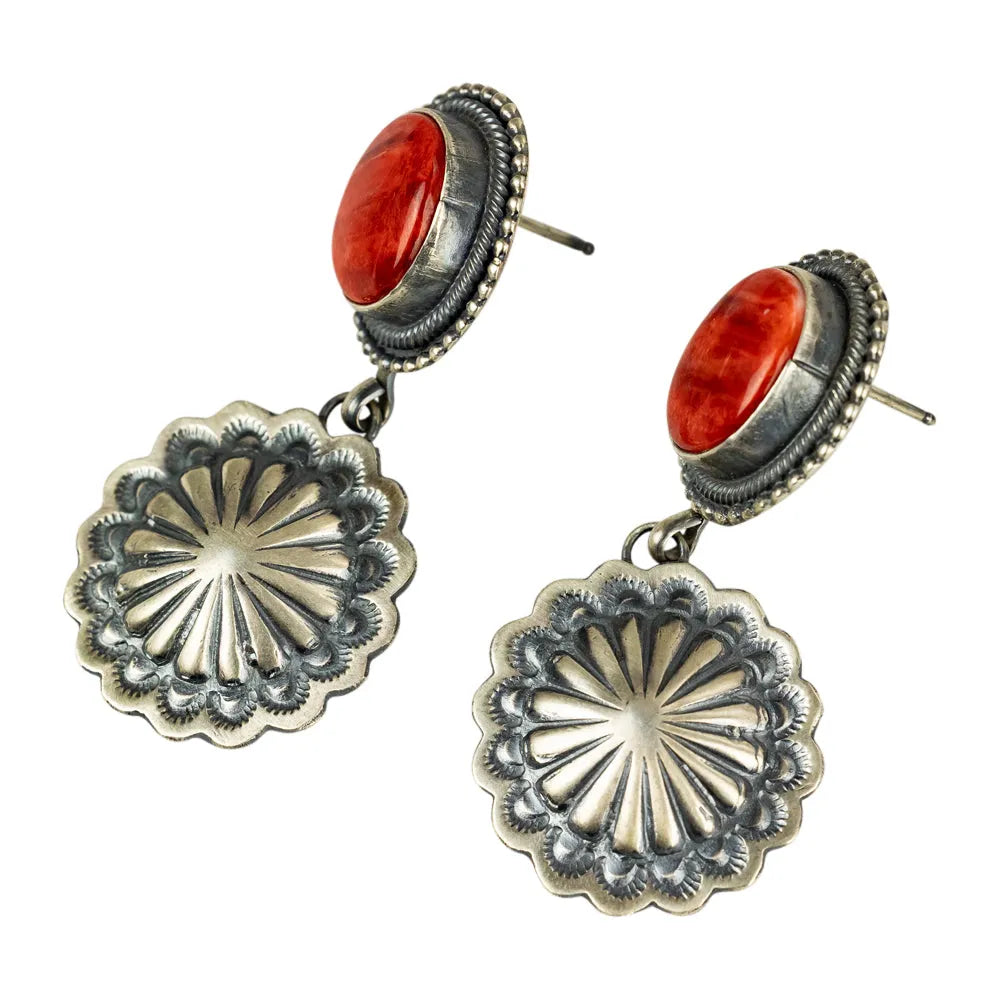 Pair of Navajo earrings with silver concho-style design and coral stone on a white background