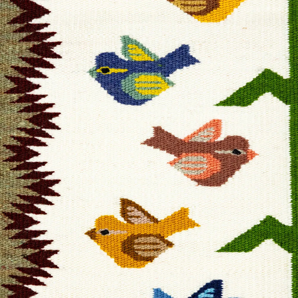 Close-up of a wool rug with colorful birds and leaves.