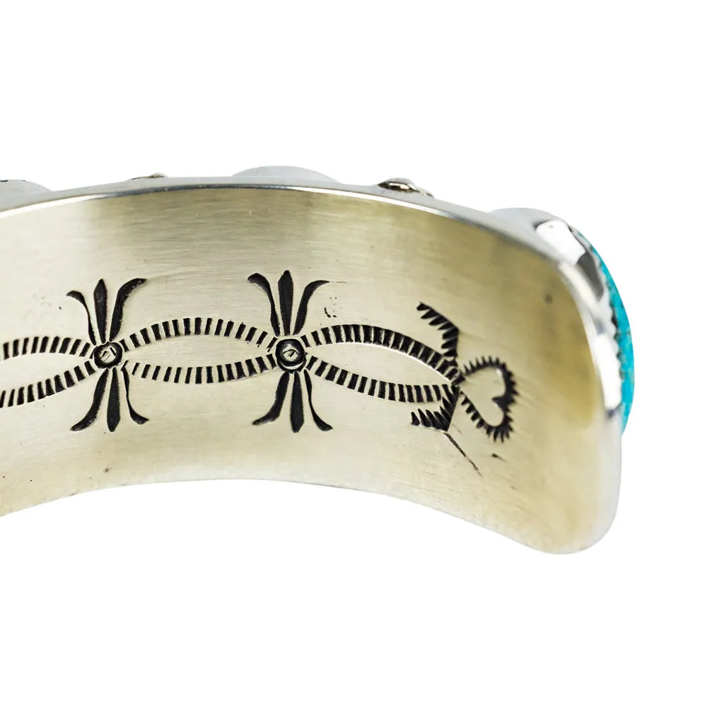 Silver bracelet with black engraved design and turquoise stone on a white background
