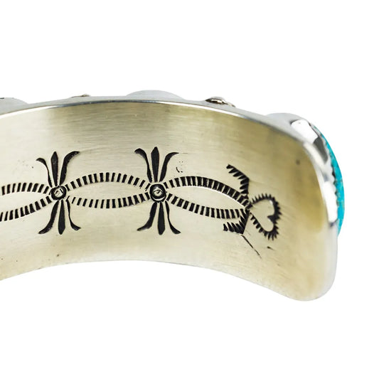 Silver bracelet with black engraved design and turquoise stone on a white background