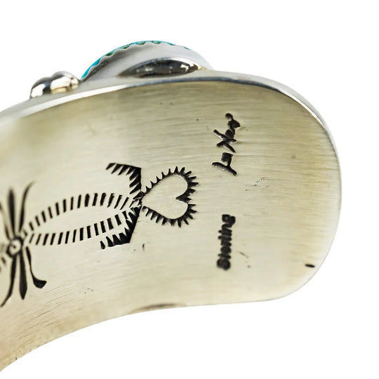 Close-up of a Navajo bracelet with hallmark and engraved designs on a white background