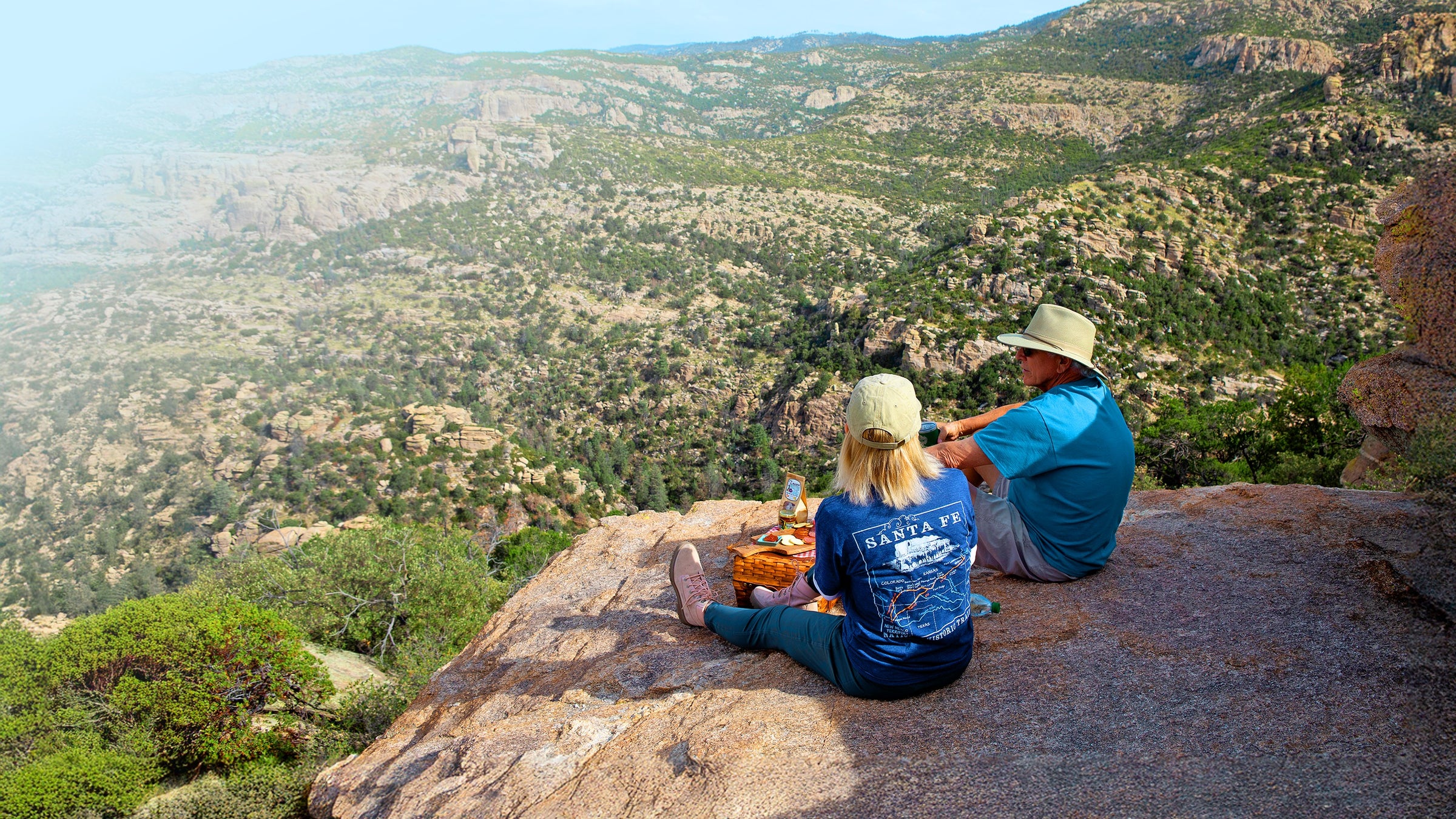 Two people sitting on a rocky outcrop overlooking a scenic landscape.