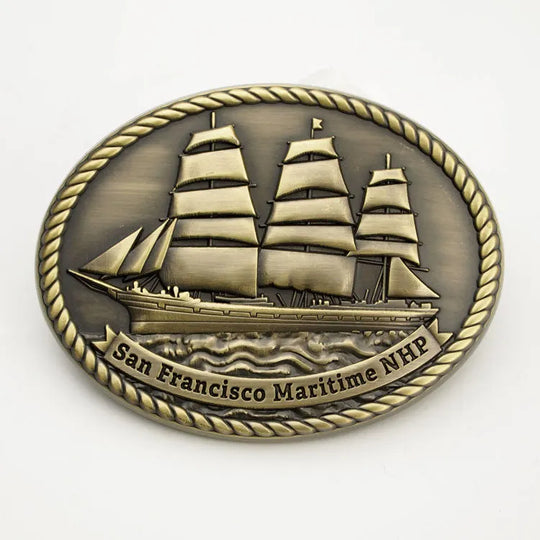 A copper colored belt buckle featuring an embossed image of a historic ship with the text 'San Francisco Maritime NHP'.