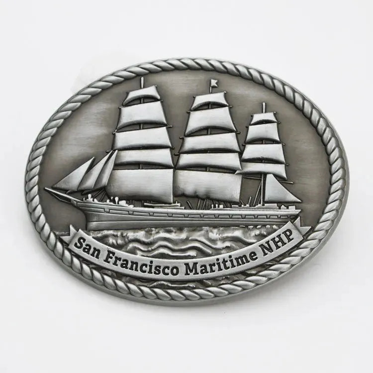 A pewter colored belt buckle featuring an embossed image of a historic ship with the text &